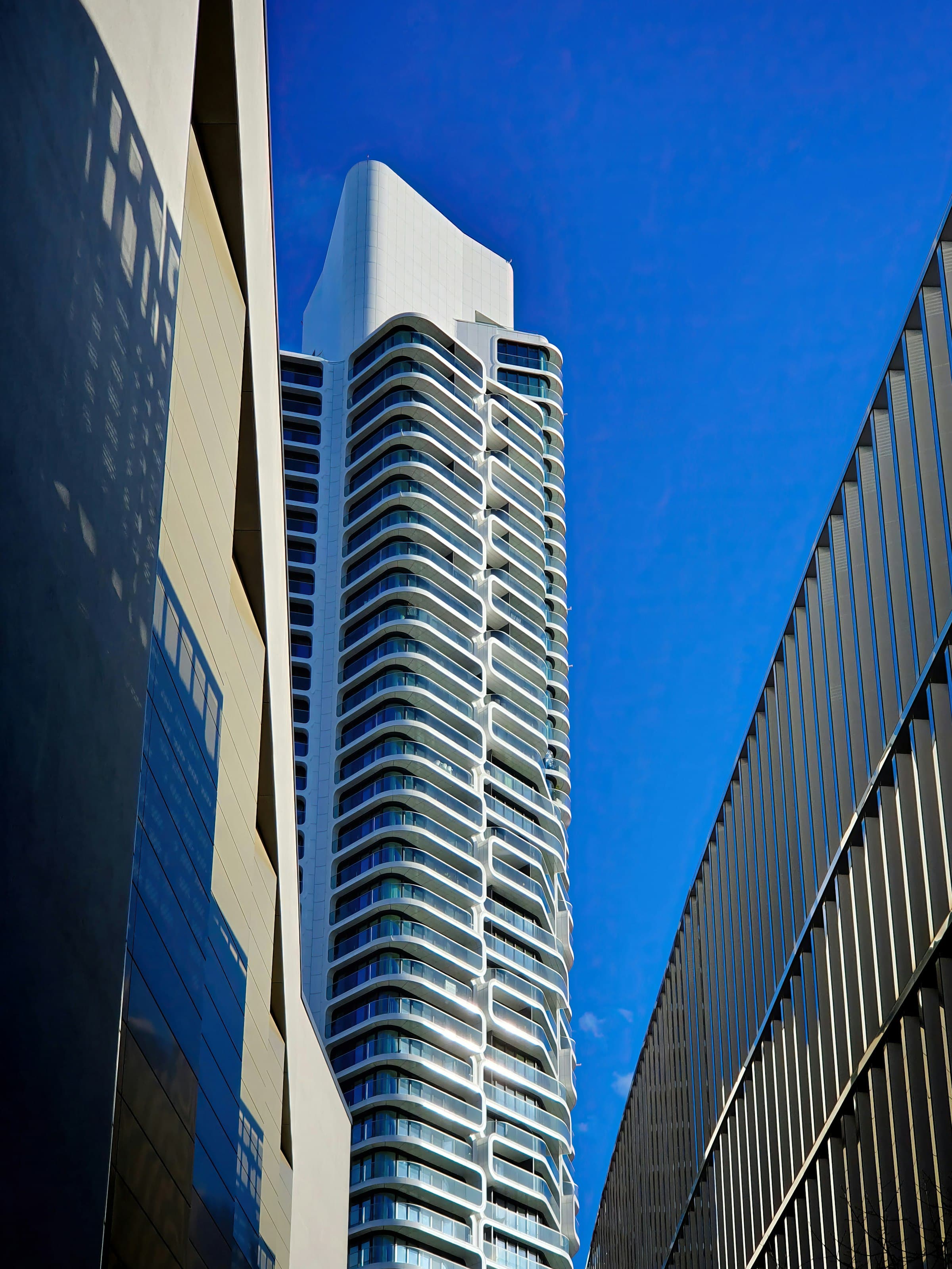 Curved white-balcony luxury tower against a blue sky